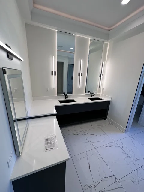 Modern bathroom with black vanity, dual sinks, illuminated mirrors, and marble tile flooring