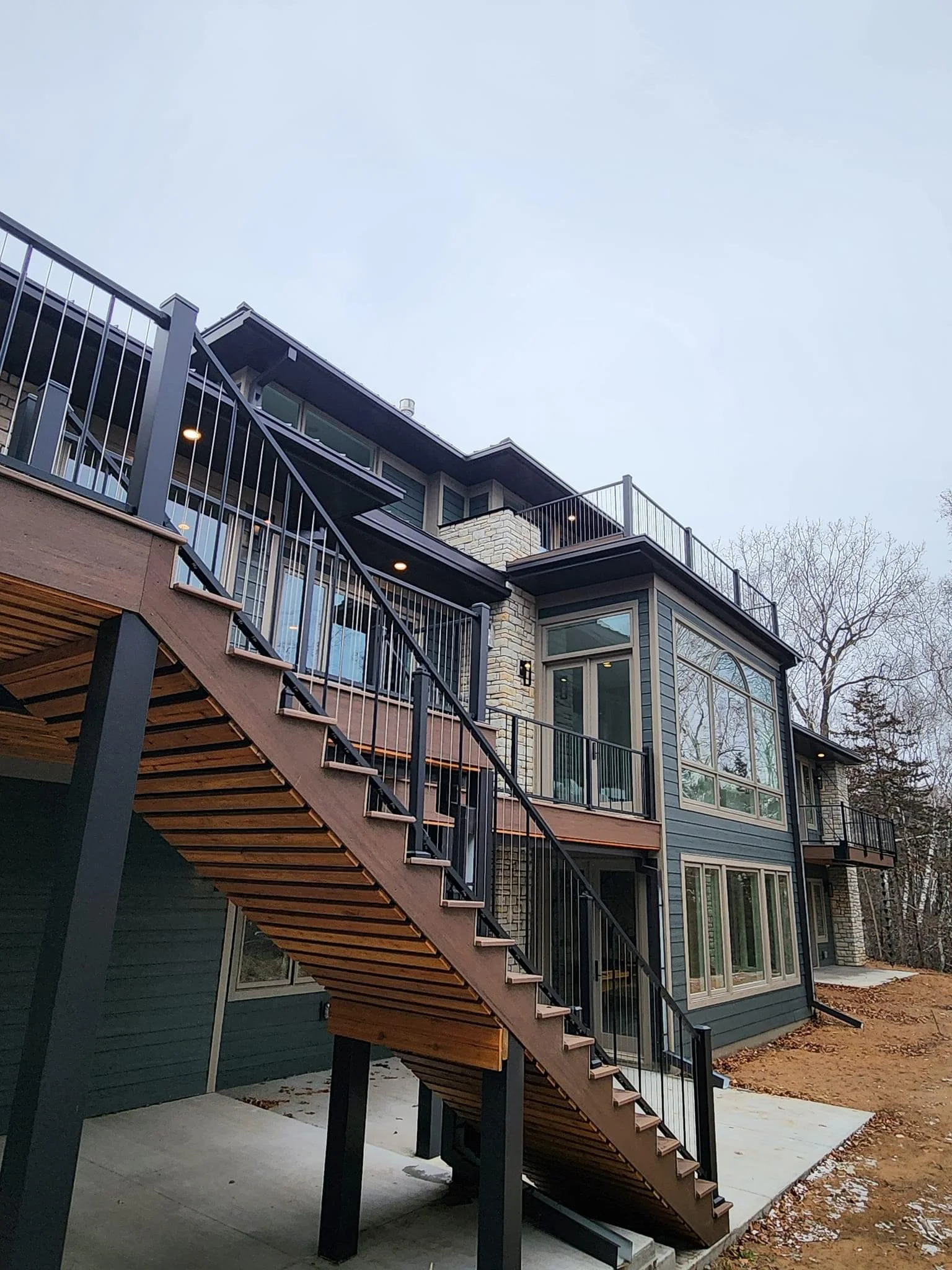 Modern home addition with wooden exterior staircase, black railings, and stone veneer facade