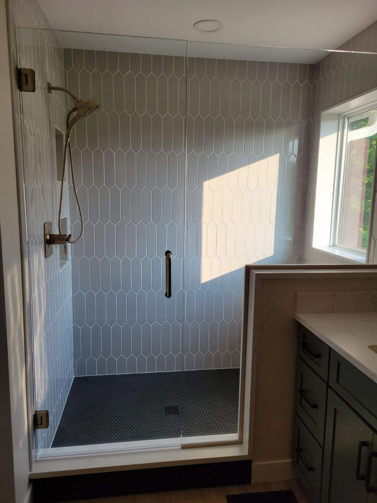 Modern bathroom shower with gray hexagonal tile walls and dark tile floor, frameless glass door