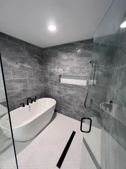 Modern bathroom with gray tile walls, white soaking tub, and walk-in shower