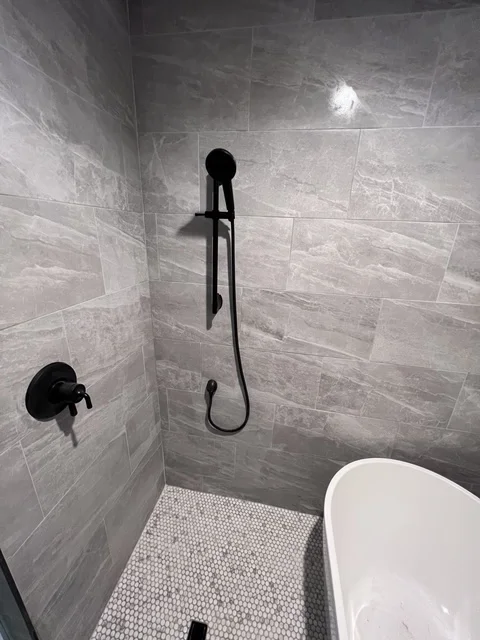 Modern bathroom shower with gray tile walls, black fixtures, and hexagonal floor tile