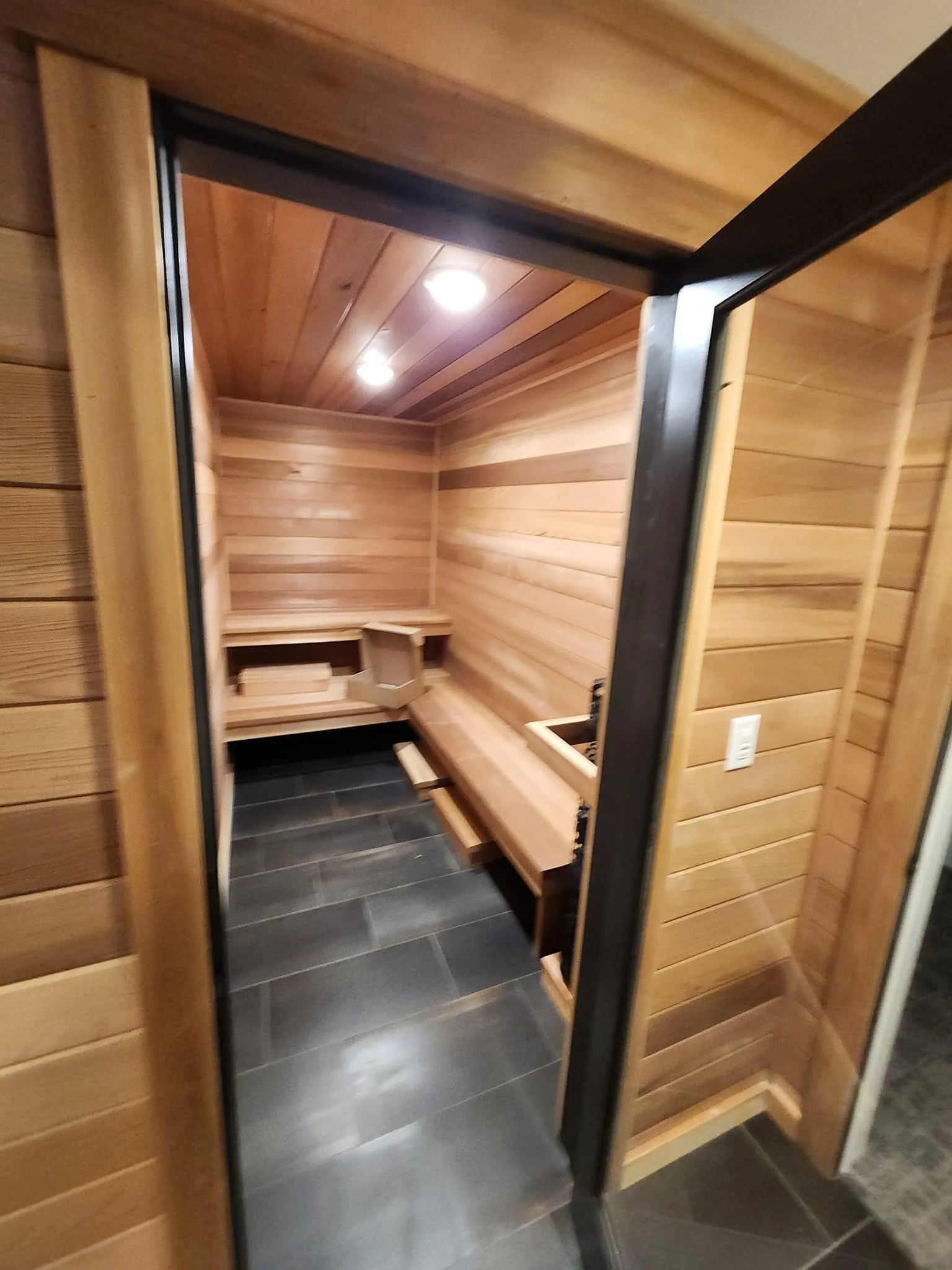 Interior view of newly installed cedar sauna with benches, LED lighting, and tile floor