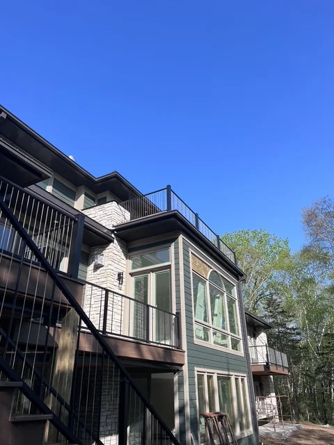Modern two-story home addition with stone and siding exterior, metal deck railing, and integrated roofline