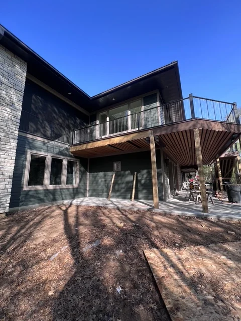 Modern two-story home addition with black exterior, deck, and concrete patio