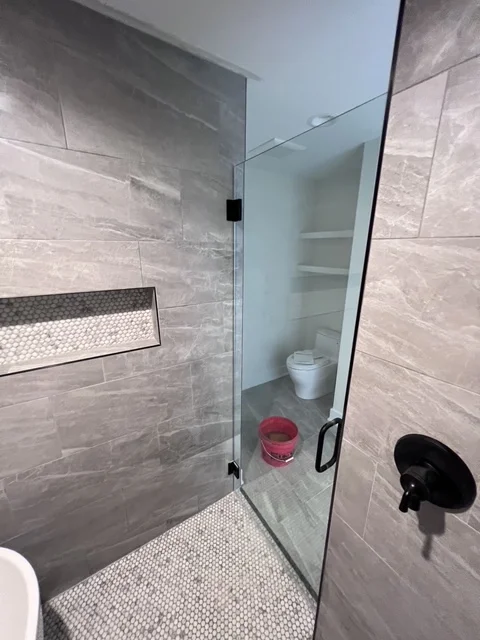 Modern gray tile shower with frameless glass door and penny tile floor