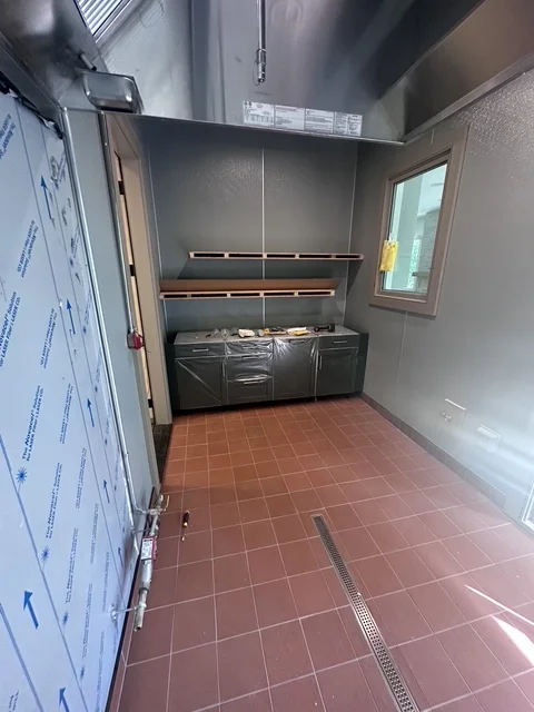 Commercial kitchen with terracotta tile floor, stainless steel hood, and black cabinetry