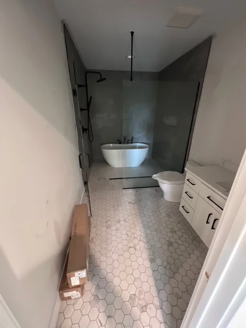Newly remodeled bathroom with hexagonal tile floor, white vanity, and dark tile walls