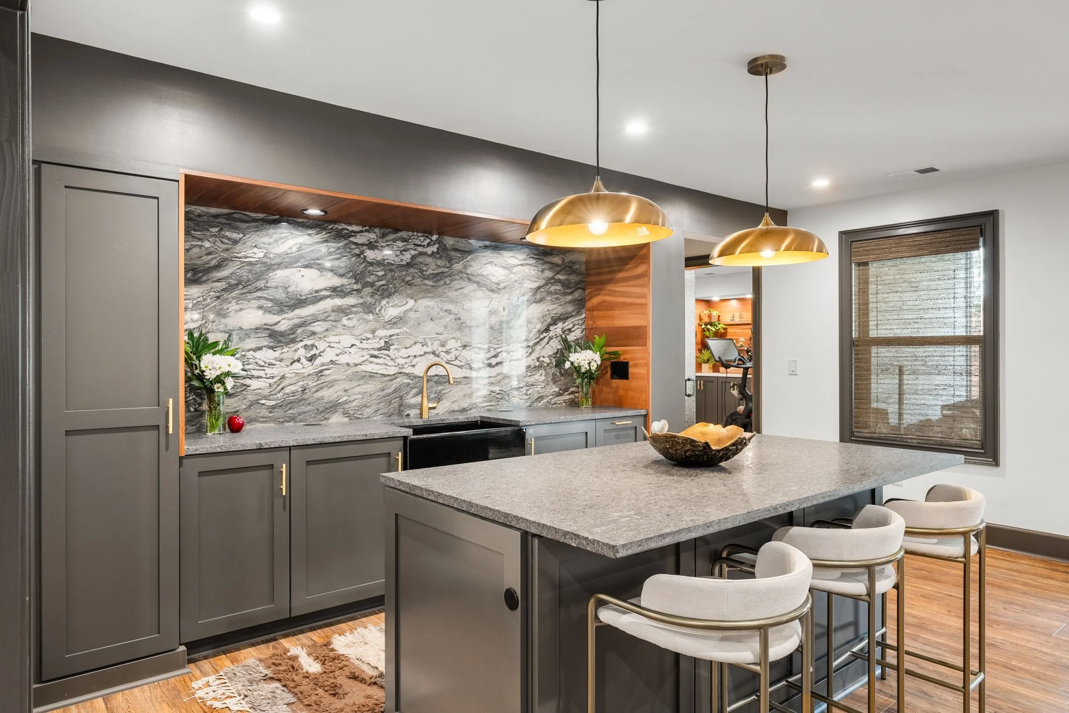 Modern kitchen with gray cabinetry, marble backsplash, quartz island, and brass pendant lights