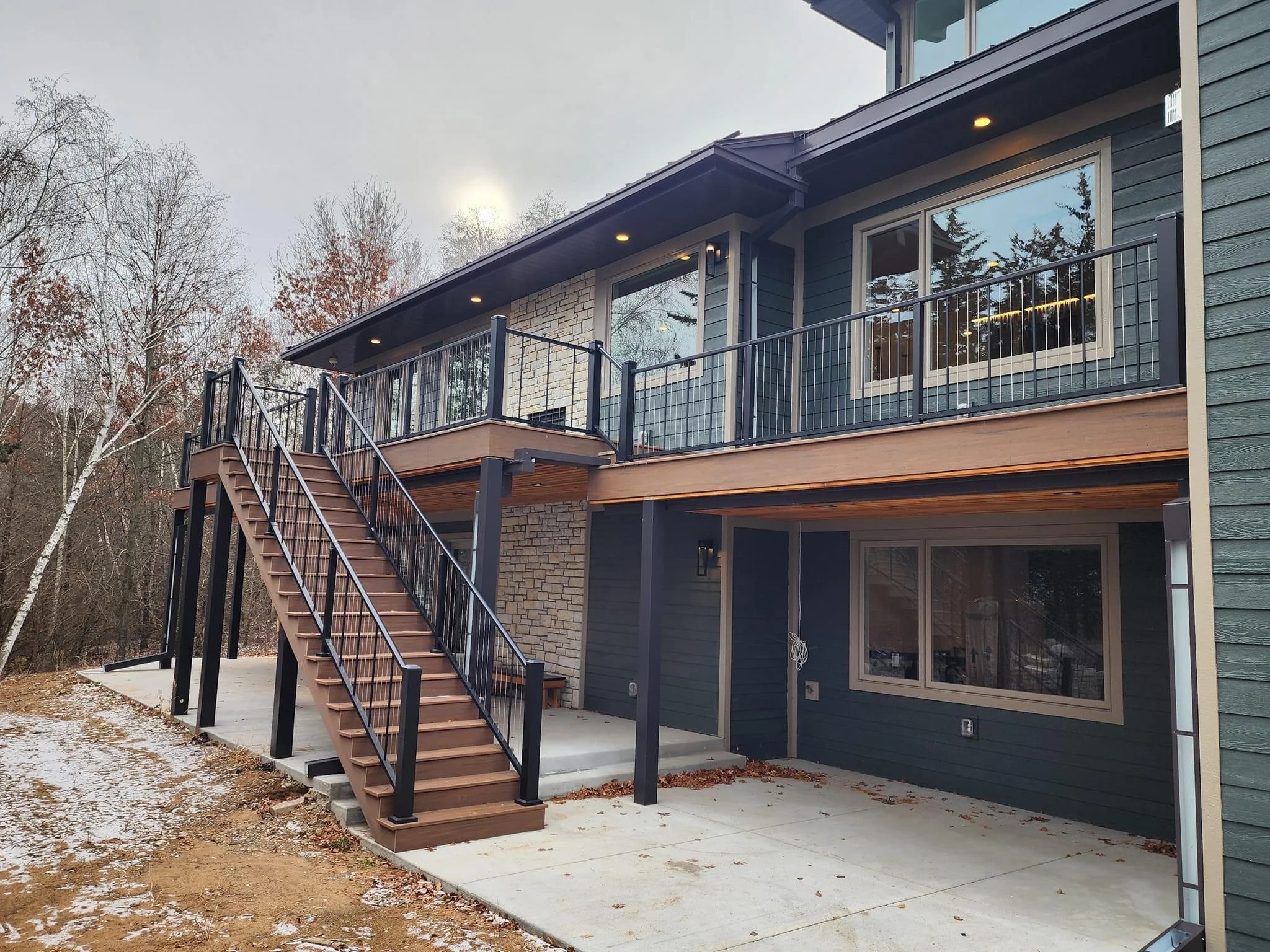 Modern two-level deck with black metal railing and composite decking overlooking wooded landscape