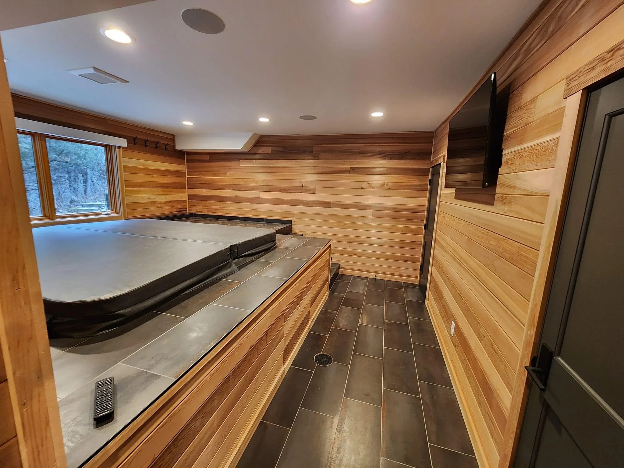 Modern home sauna with cedar wood walls, tiered seating, slate flooring, and picture window