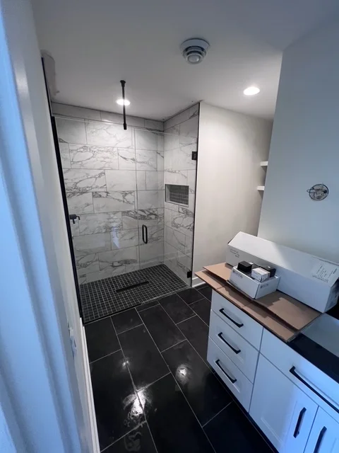 Modern bathroom with frameless glass shower, marble tiles, black flooring, and white vanity