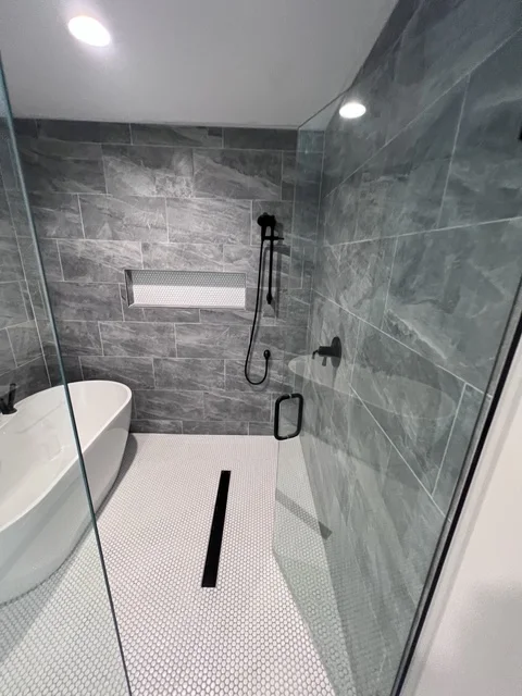 Modern bathroom with gray tile walk-in shower, frameless glass doors, and white hexagonal floor tile