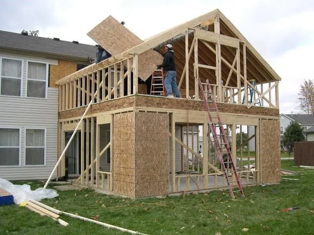 Two-story wood-framed home addition under construction with exposed framing and deck