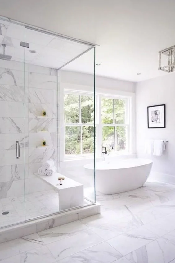 Bright modern bathroom with marble flooring, glass shower enclosure, and white soaking tub