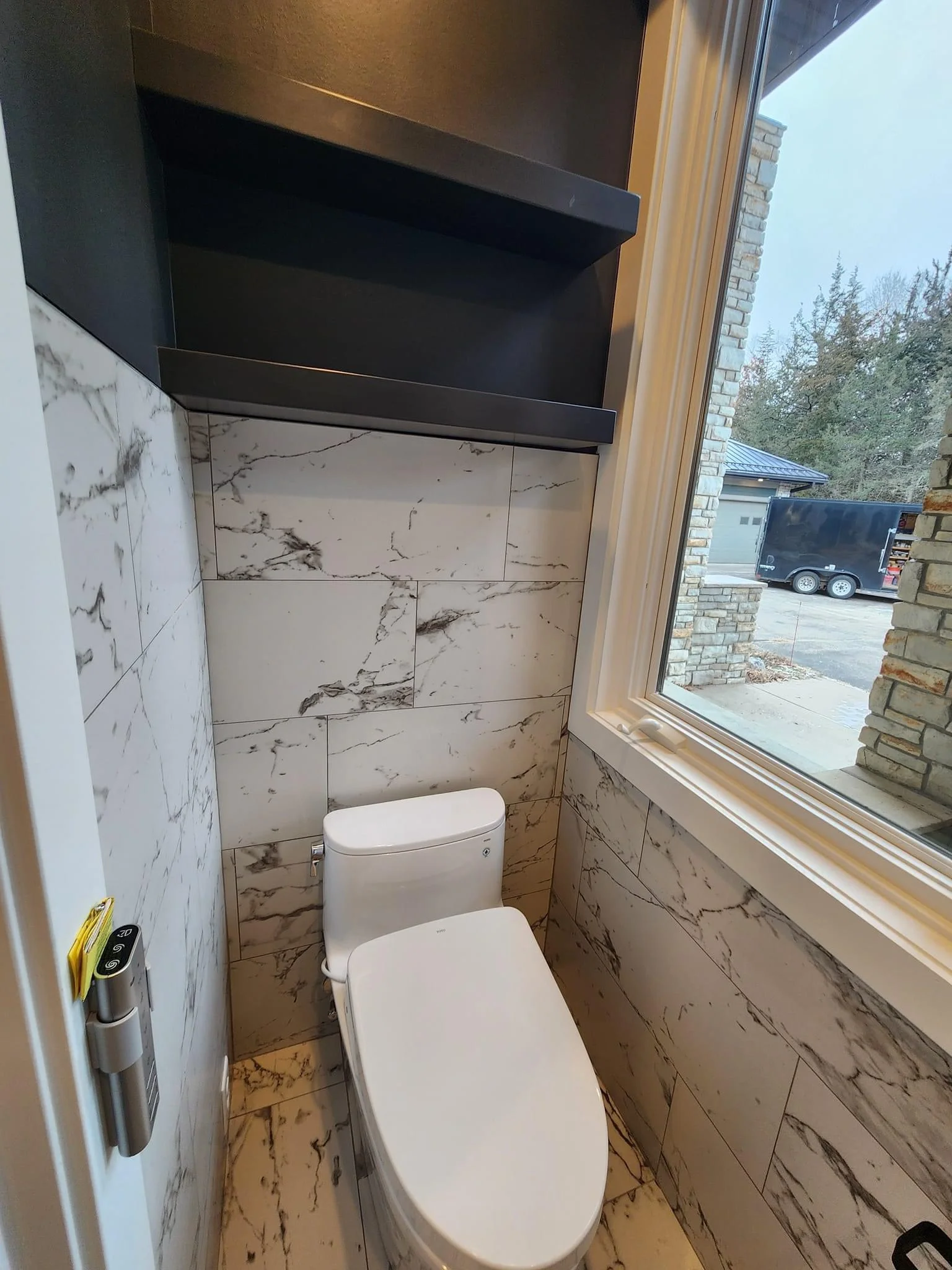 Modern bathroom with marble-look tile walls, white toilet, black vanity, and large window