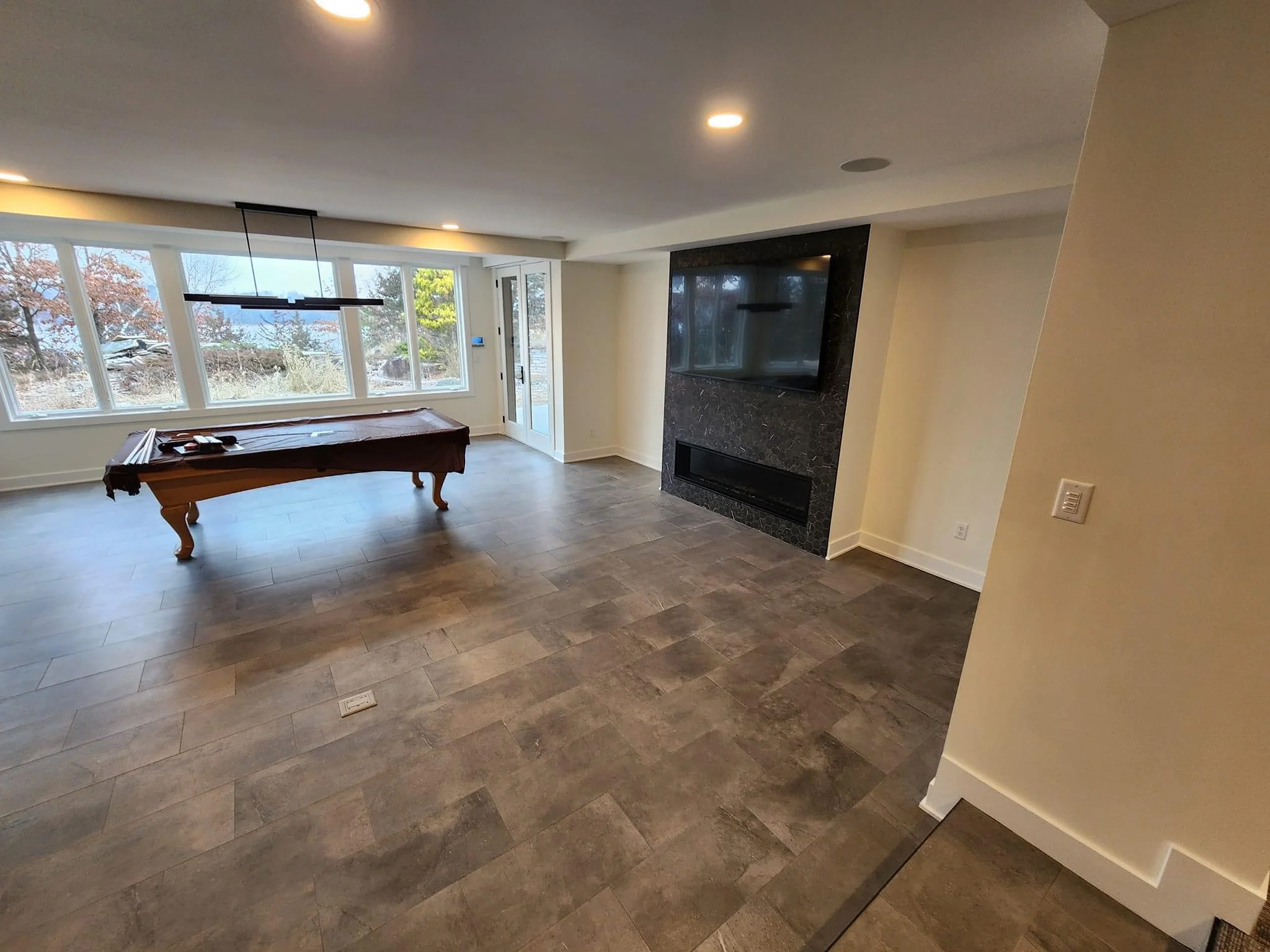 Recreation room with herringbone tile flooring, stone fireplace, and large windows