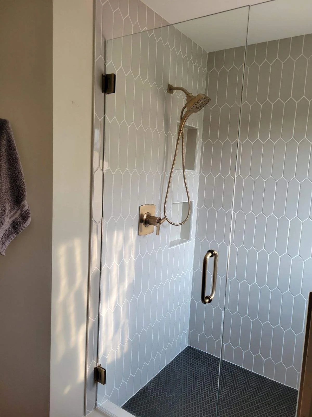 Modern shower enclosure with white hexagonal tile walls and bronze fixtures