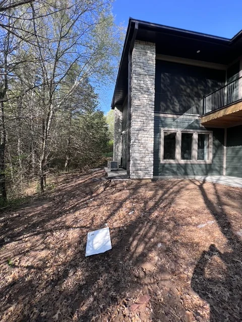 Modern stone exterior home addition with large windows and deck in wooded setting