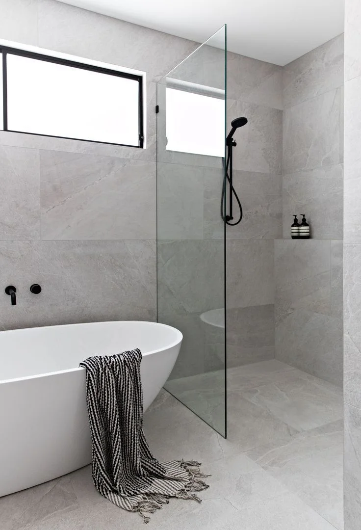 Modern bathroom with gray tile, frameless shower, and white soaking tub