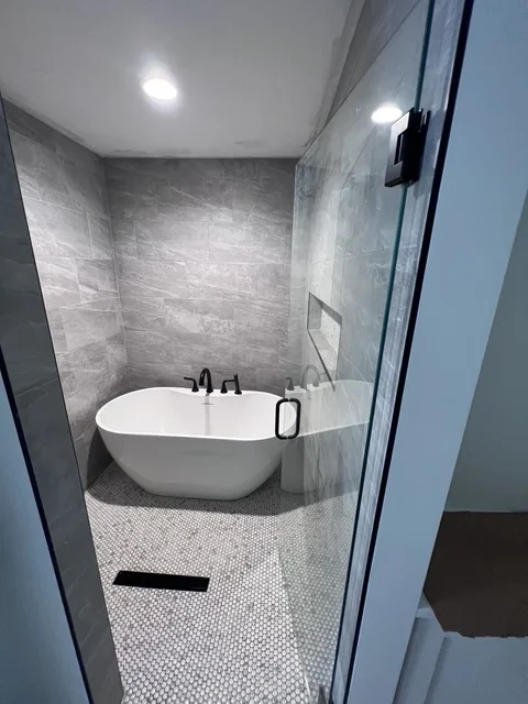 Modern bathroom with white freestanding tub, gray tile walls, and geometric floor tiles