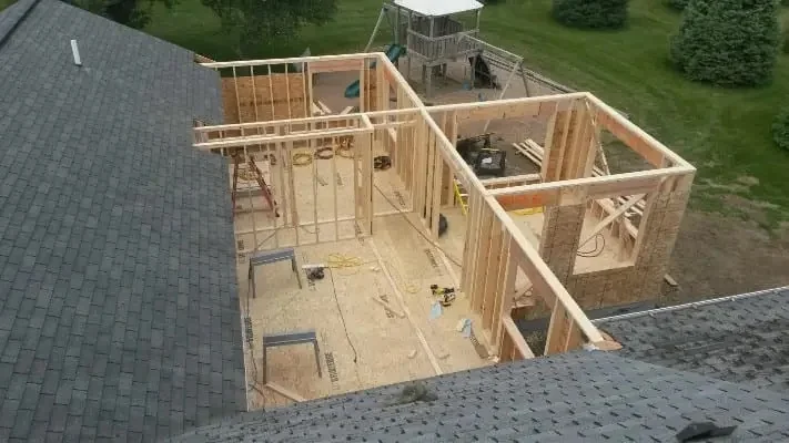 Aerial view of home addition framing with wooden studs, roof trusses, and interior walls under construction