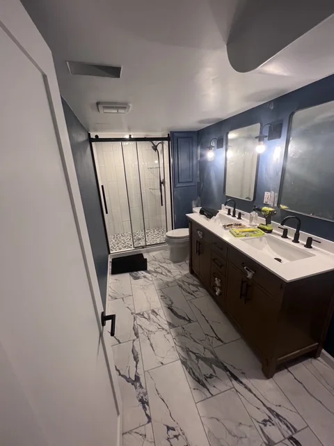 Modern bathroom with dark vanity, marble tile floor, and glass shower enclosure