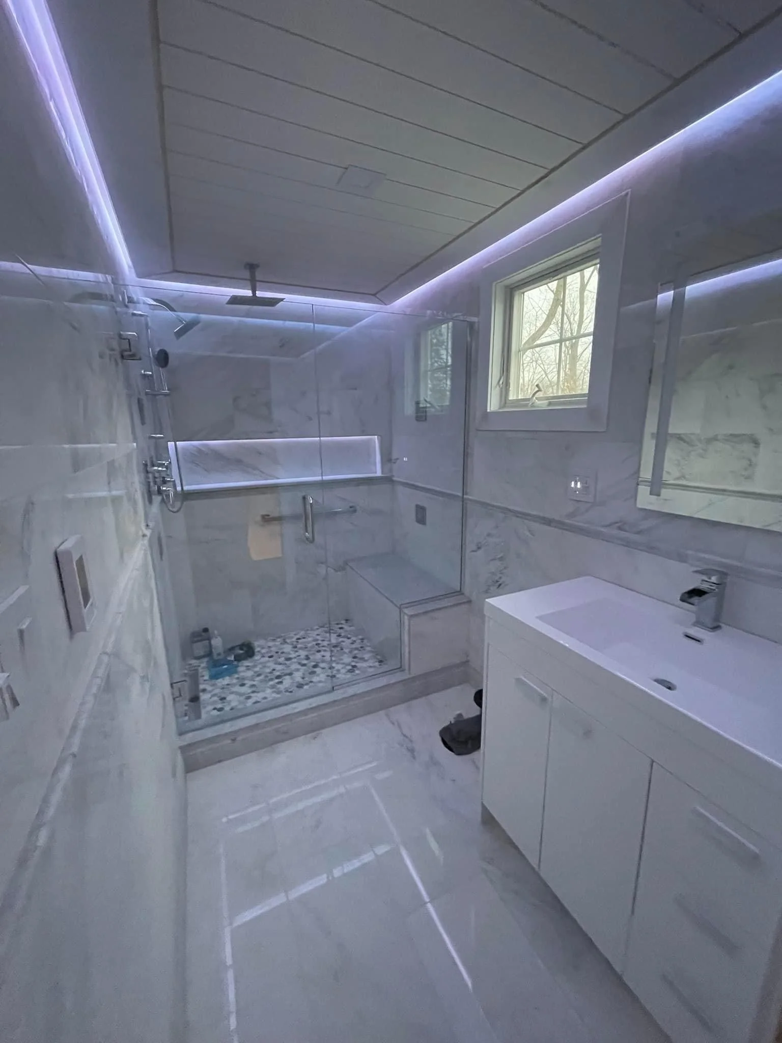 Modern bathroom with frameless shower, white vanity, marble tile, and LED ceiling lighting