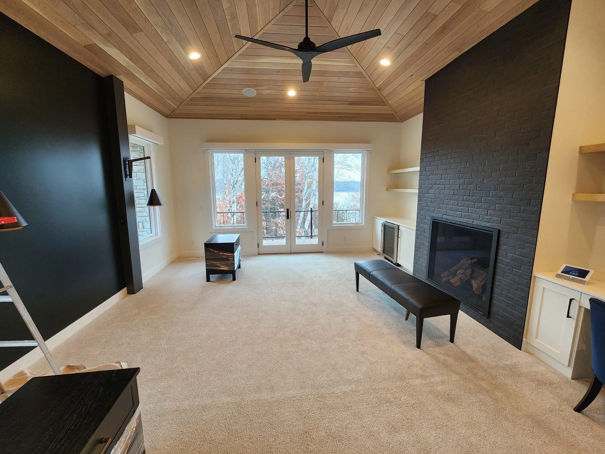 Spacious bedroom with vaulted wood ceiling, fireplace, and French doors overlooking lake