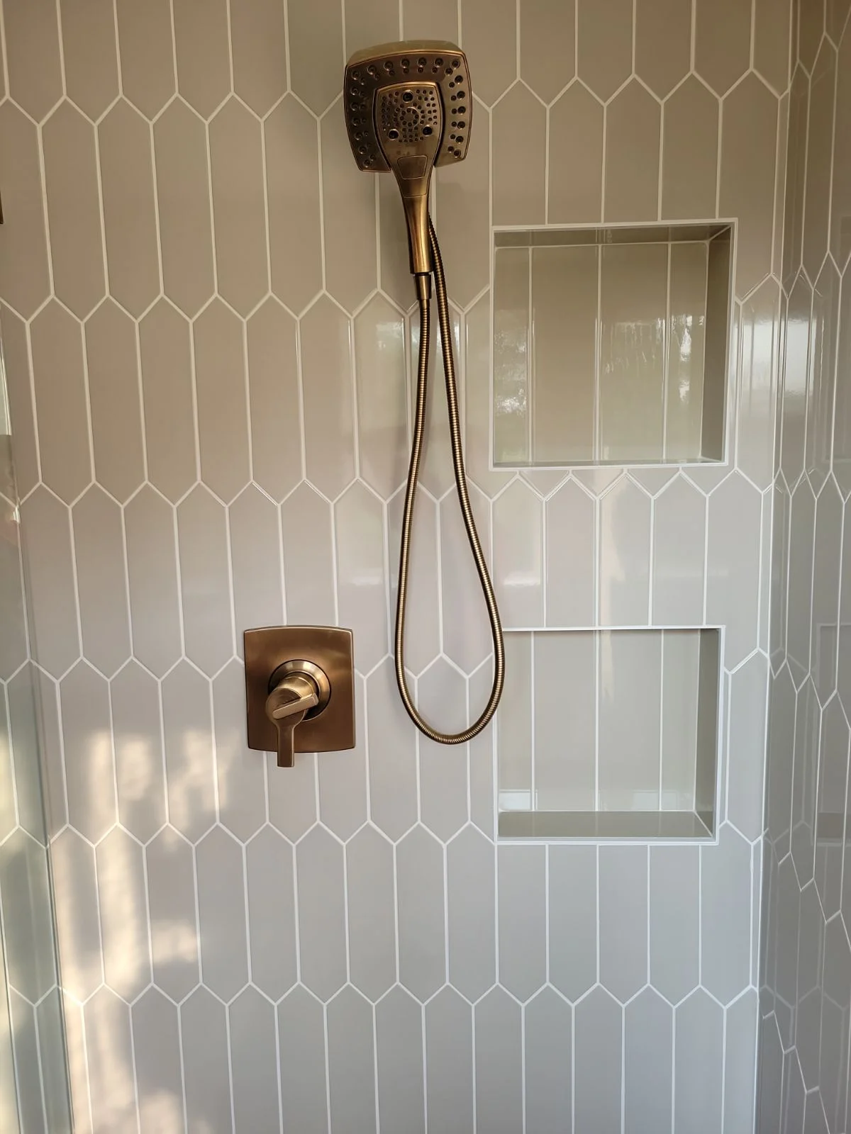 Shower with white hexagon tile walls, bronze fixtures, and frameless glass enclosure
