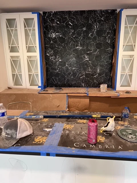 Kitchen remodeling in progress with white glass-front cabinets and black marble countertop installation