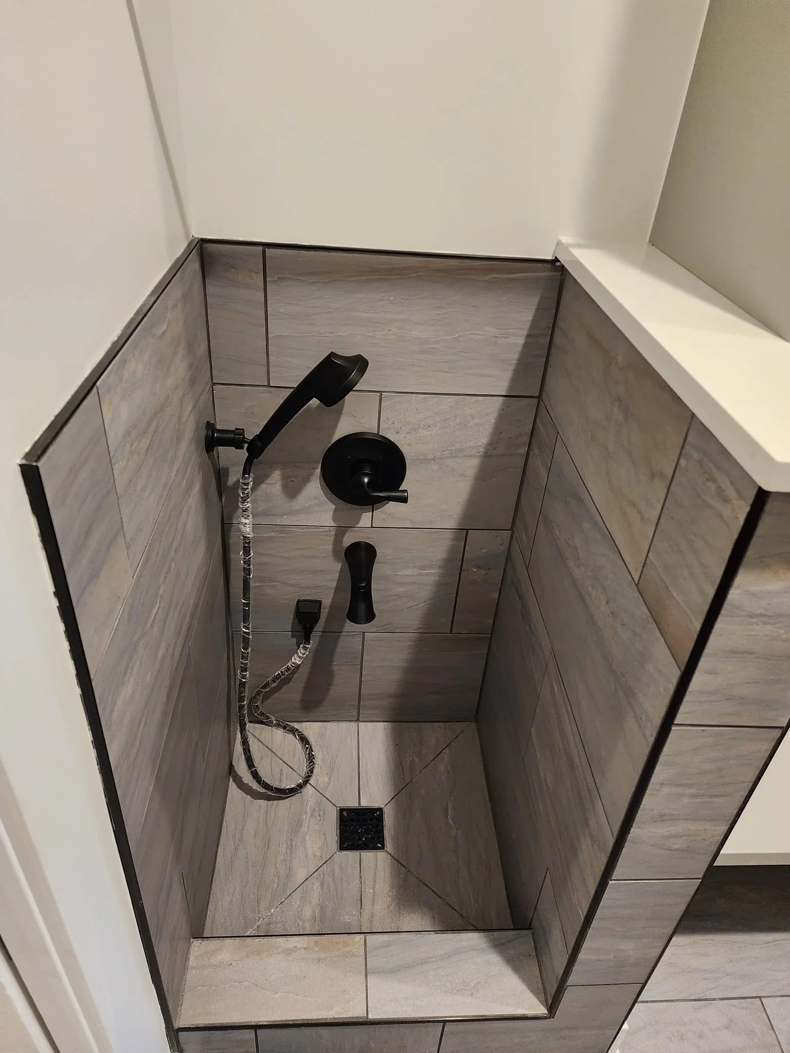 Modern shower with gray wood-look tile, black fixtures, and rainfall showerhead