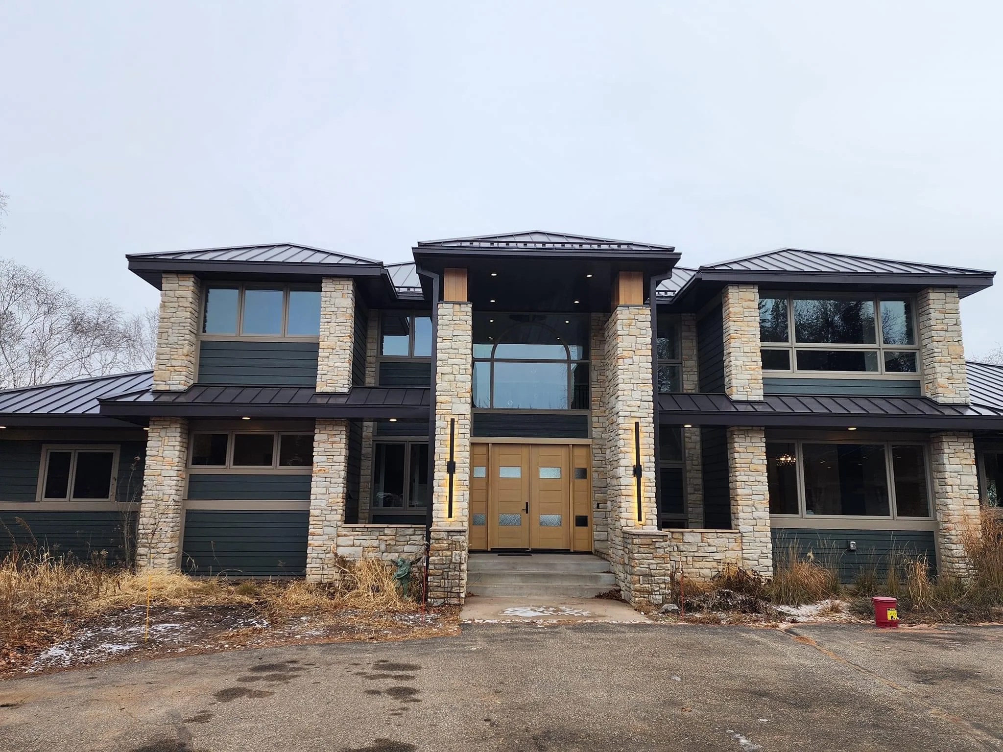 Modern two-story home with stone pillars, black metal roof, and contemporary wood entry doors
