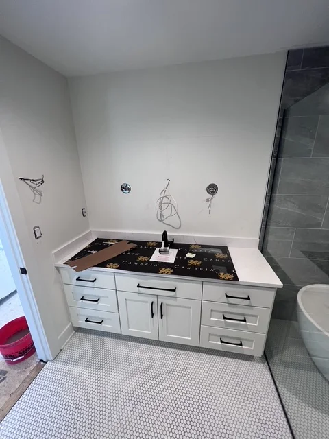 Modern bathroom vanity with white cabinetry, black granite top, and hexagonal floor tile