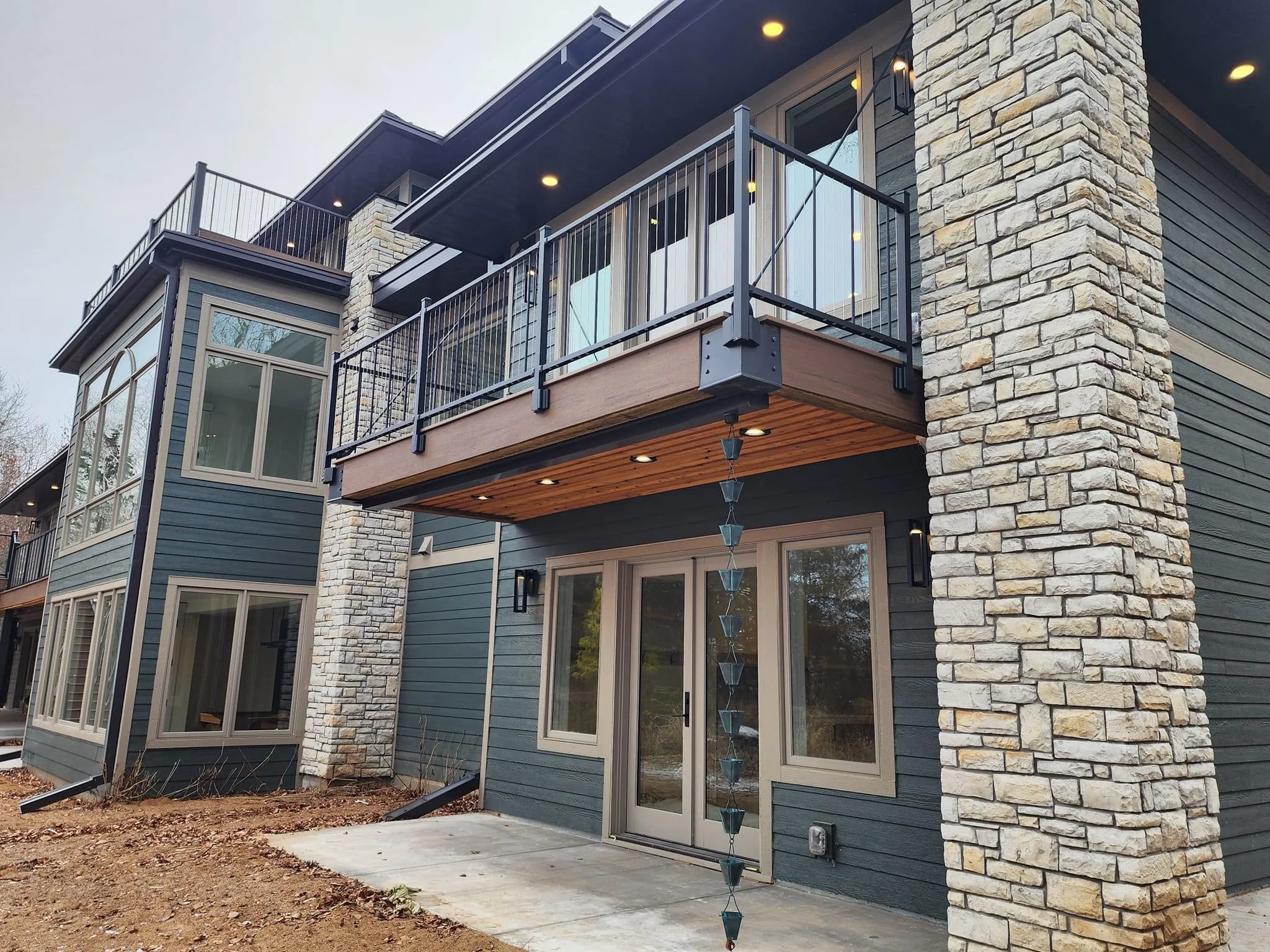 Two-story home addition with stone columns, blue siding, and modern deck railing