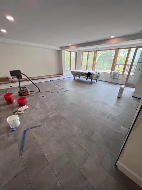 Large gray tile flooring installation in progress with layout guides and white walls