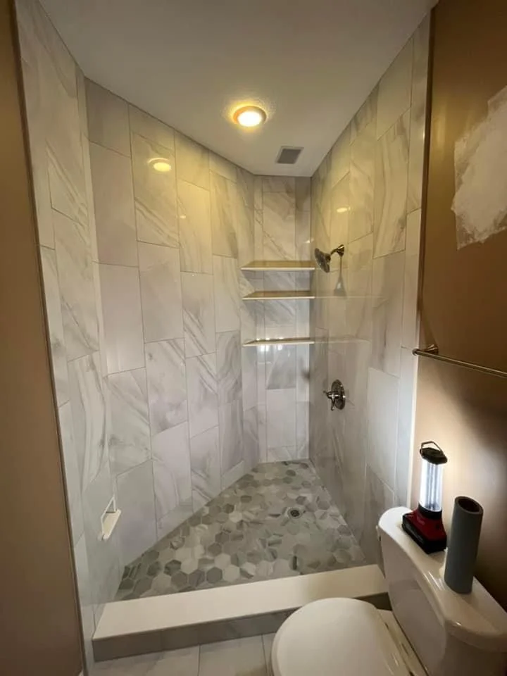 Modern bathroom shower with marble tile walls, pebble floor, and recessed lighting