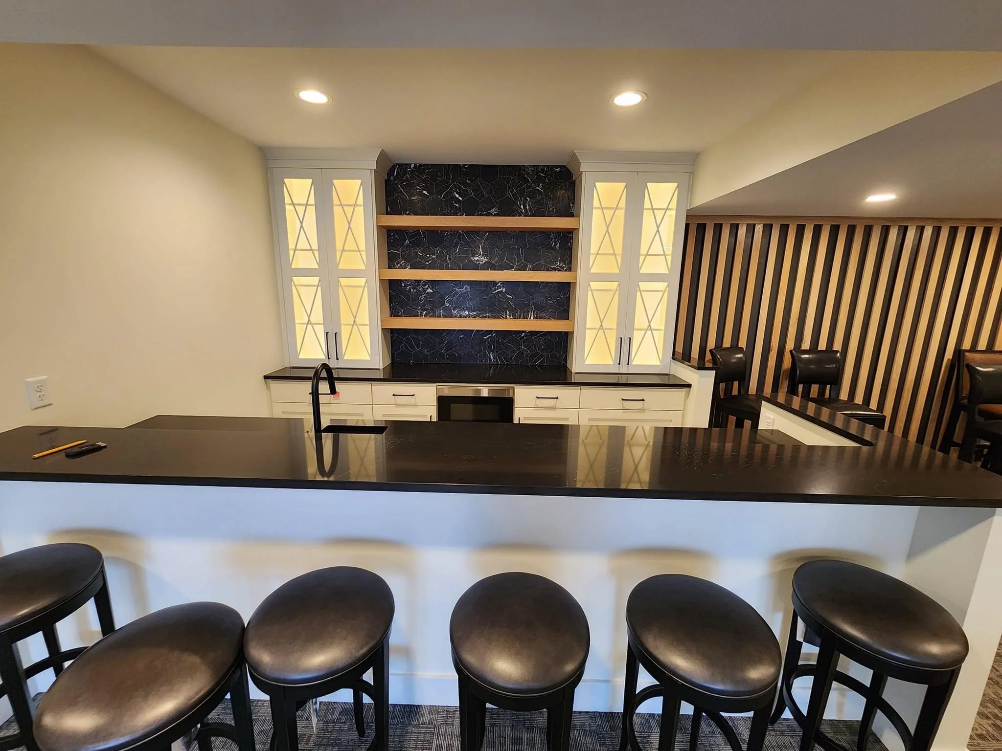 Modern home bar with white cabinetry, black quartz countertop, and marble backsplash with wood shelves