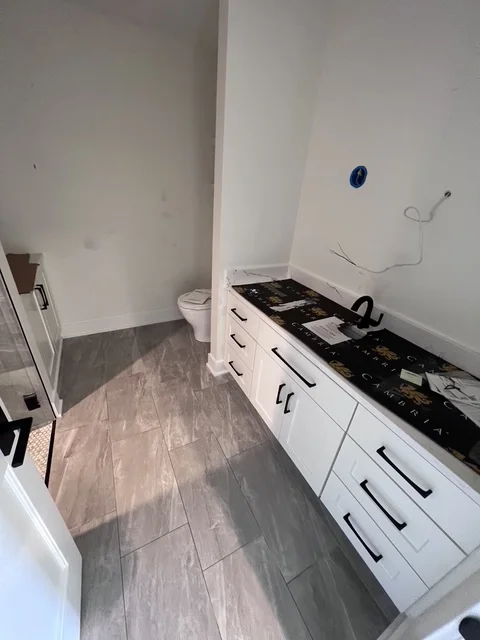 Modern white bathroom vanity with black countertop and gray wood-look vinyl flooring
