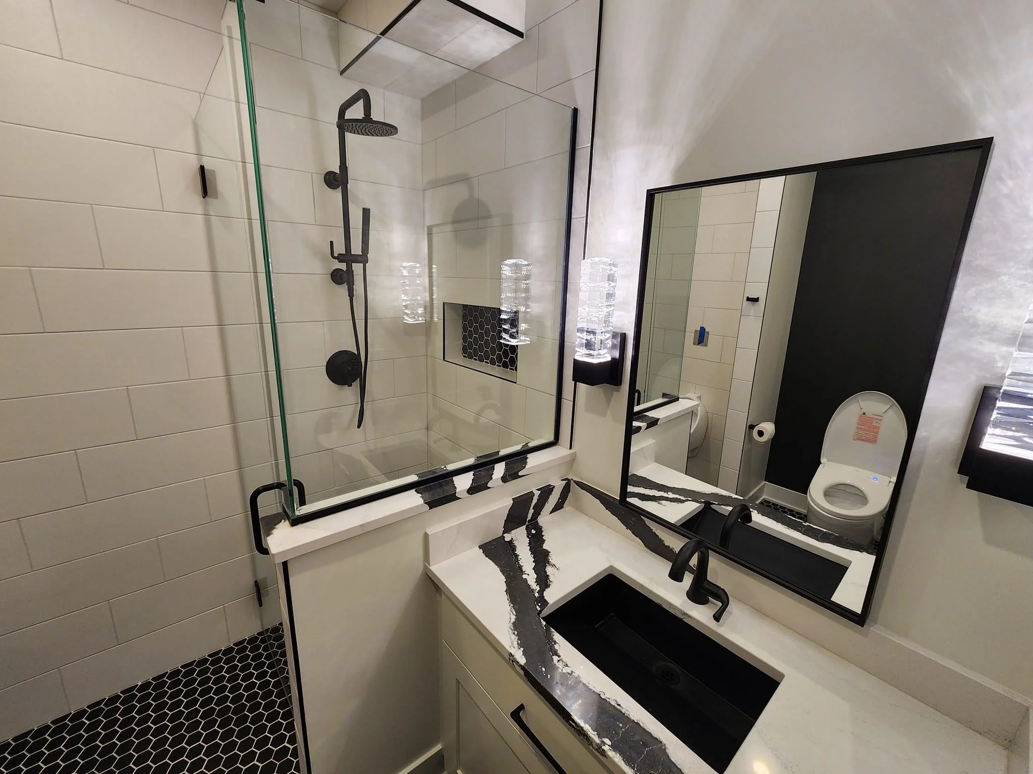 Modern bathroom with white subway tile, black hexagonal floor, frameless shower, and floating vanity