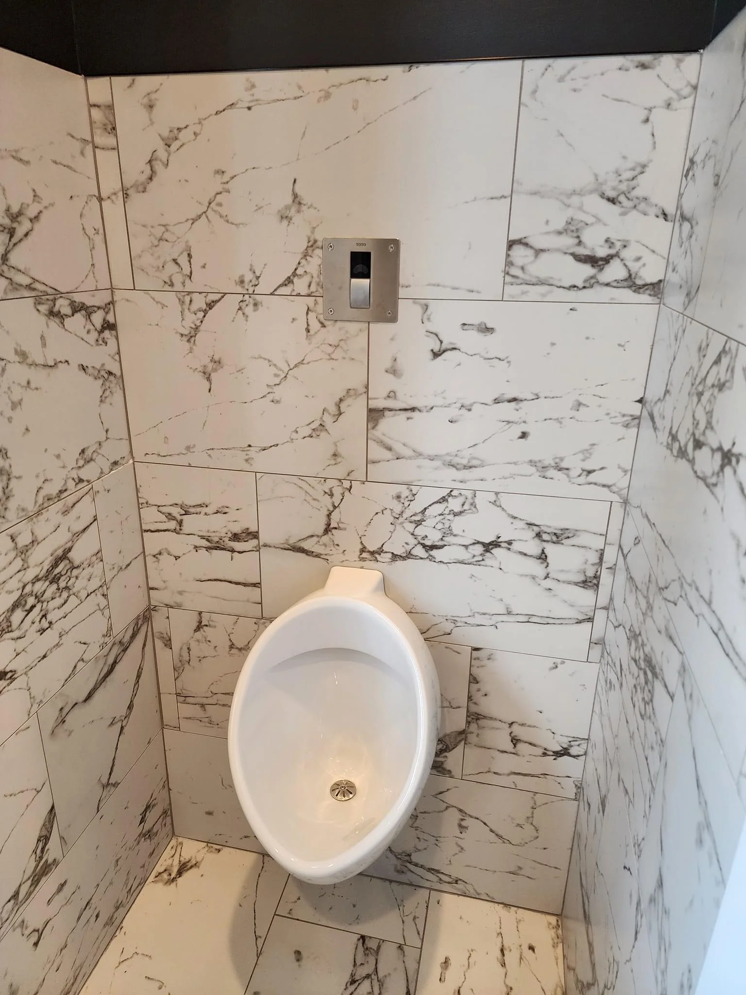 Bathroom with marble tile walls and floor, white oval toilet, and modern outlet