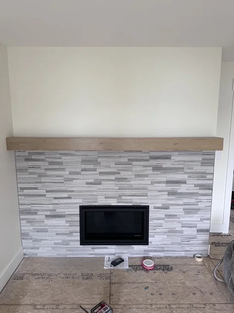 Modern fireplace with gray linear tile surround, wood mantel, and recessed TV opening