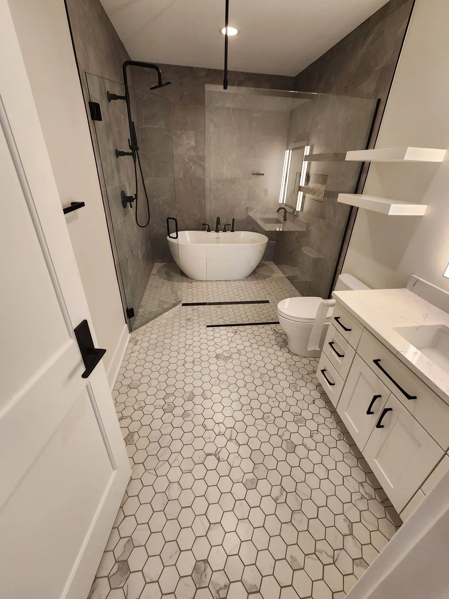 Modern bathroom with white soaking tub, gray tile shower, and hexagonal marble flooring
