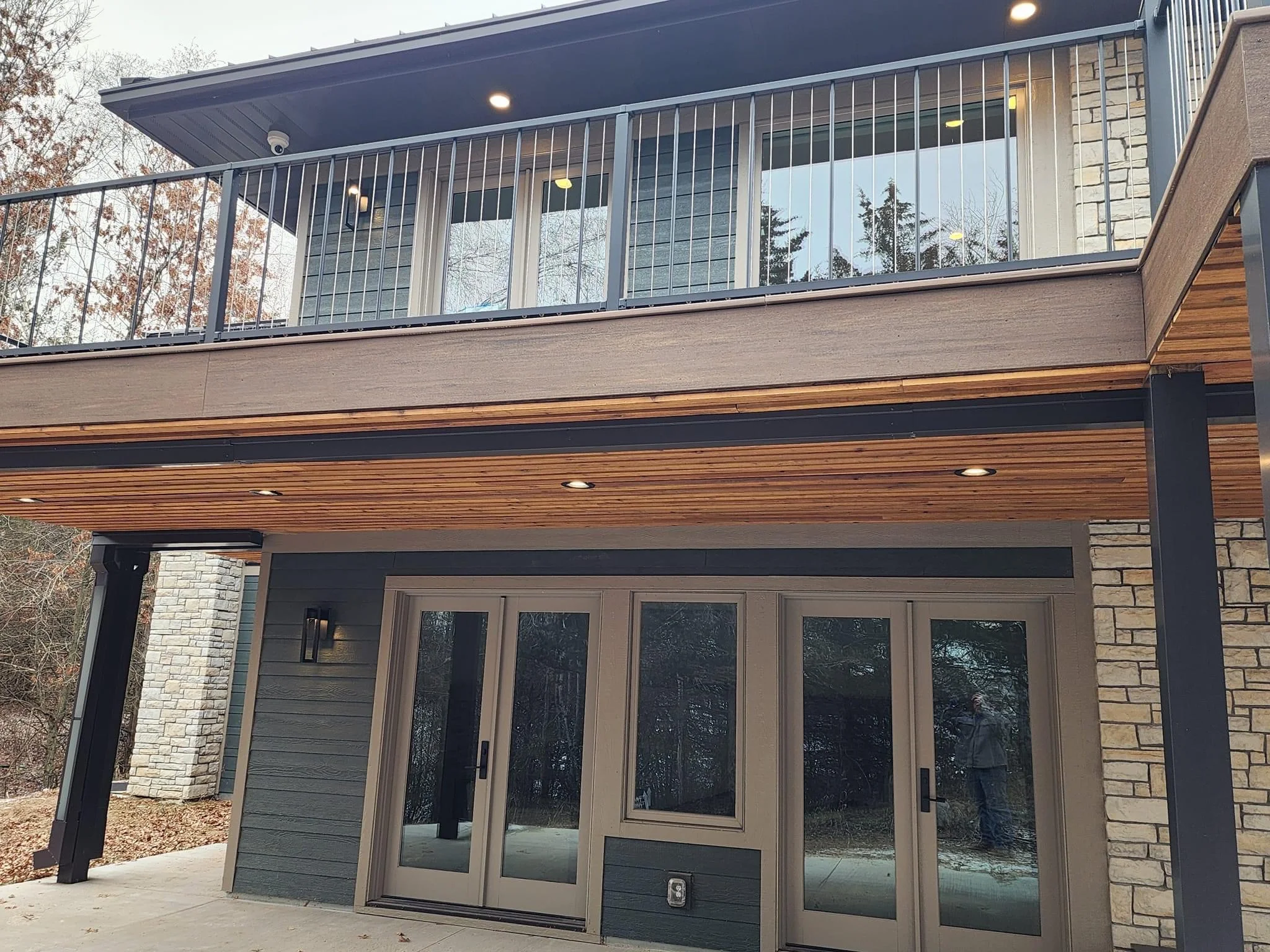 Two-story modern home addition with upper deck, glass railings, wood soffits, and new garage